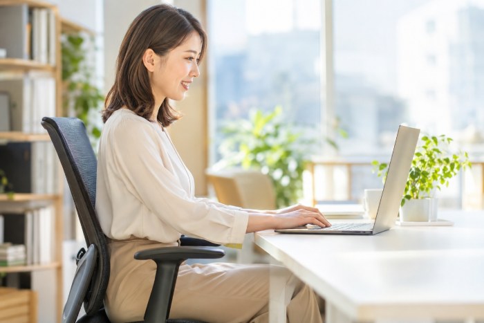 明るいオフィスで、背すじが自然に伸びた姿勢で集中して仕事をする女性