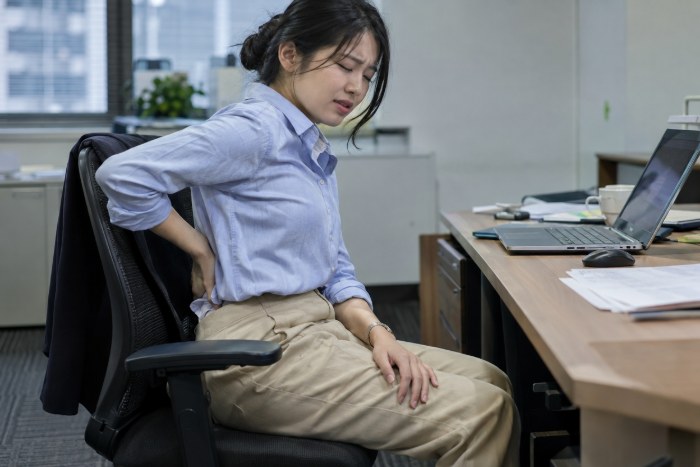 長時間のデスクワークのあと、腰に手を当てる女性